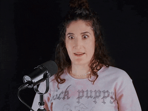 a woman wearing a pink sweater that says sick puppies salutes in front of a shure microphone