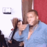 a man in a blue shirt is dancing in a room with a woman behind him .