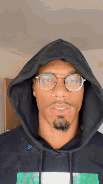 a man wearing glasses and a hooded sweatshirt looks at the camera