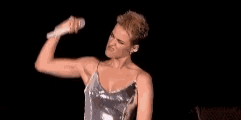 a woman in a silver dress is holding a microphone and flexing her muscles on a stage .