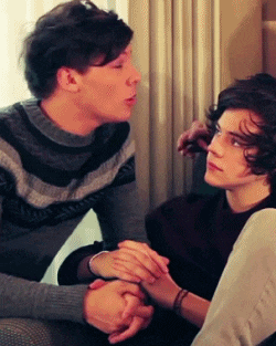 two young men are sitting on a couch holding hands and looking at each other