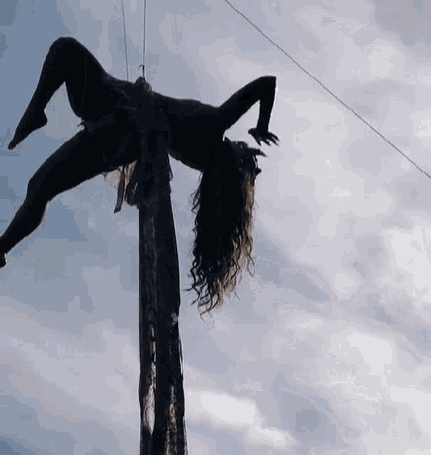 a woman is doing aerial acrobatics on a rope against a cloudy sky .