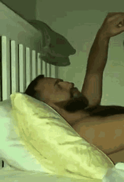a shirtless man with a beard is laying in bed with his arms outstretched .
