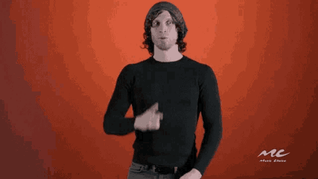 a man in a black sweater and hat is making a shhh sign with his finger on his lips .
