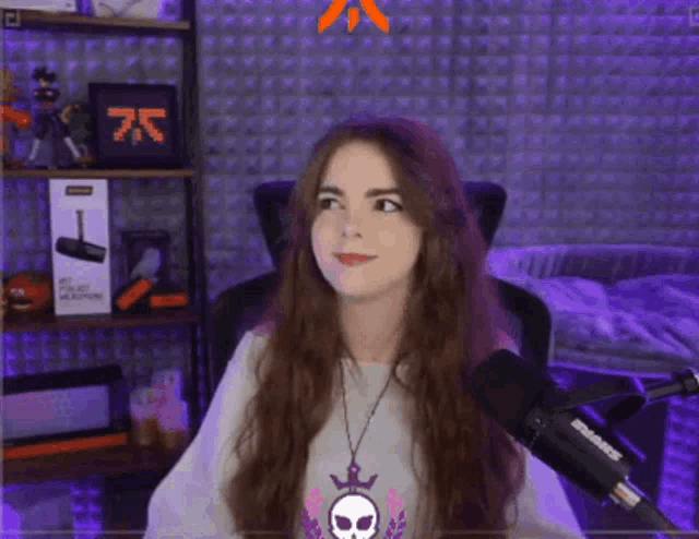 a woman sitting in front of a shure microphone with a skull necklace around her neck