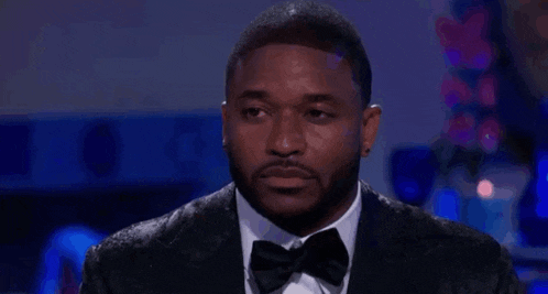 a man in a tuxedo and bow tie is looking down at something .