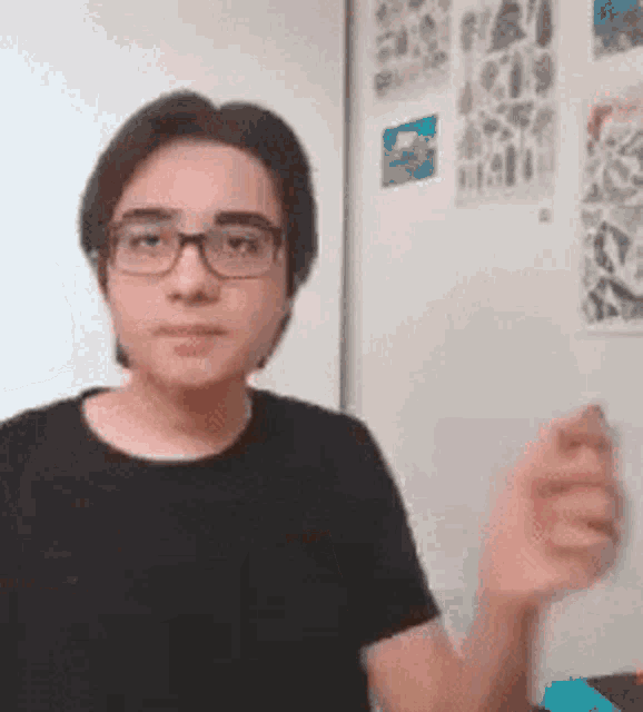 a young man wearing glasses and a black shirt is standing in a room .
