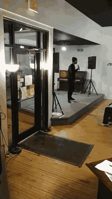 a man stands on a stage in a room with an exit sign above him