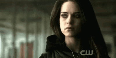 a close up of a woman 's face in a dark room with a cw logo in the background .