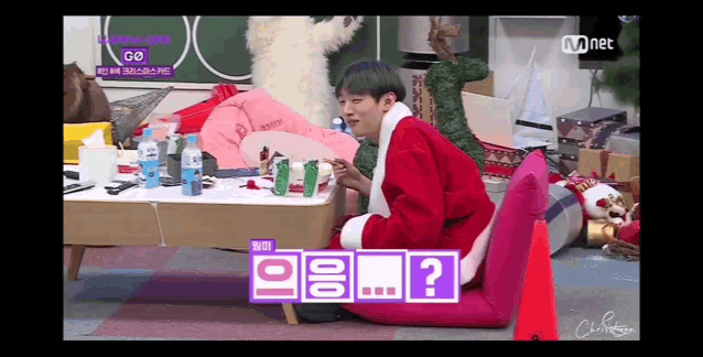 a man in a santa suit is sitting on a couch with a question mark on the screen