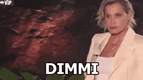 a woman in a white jacket and white tank top is standing in front of a wall with the words dimmi written on it .