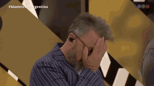 a man covering his face with his hand in front of a masterchef argentina logo