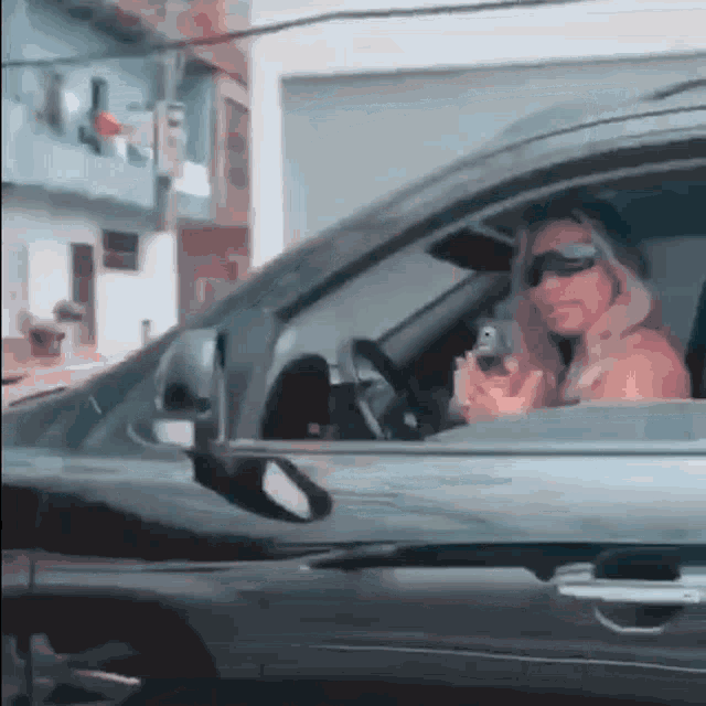 a woman is sitting in the driver 's seat of a car looking at her phone .