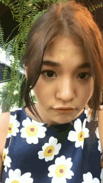 a woman wearing a blue top with white and yellow flowers makes a face