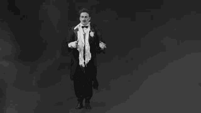 a black and white photo of a man in a tuxedo standing on a black background .