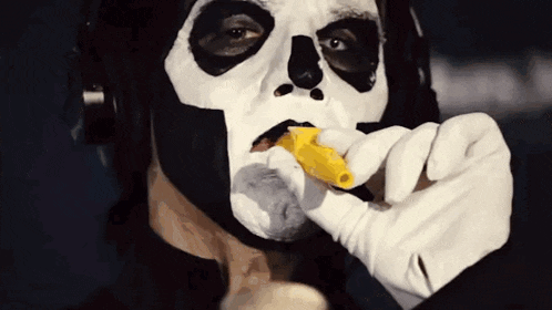 a man wearing a skeleton mask and white gloves is eating a banana