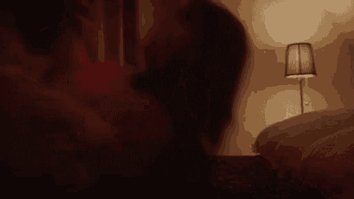 a person is laying on a bed in a dark room with a lamp in the background .