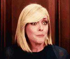 a woman with blonde hair and a black shirt is making a funny face .