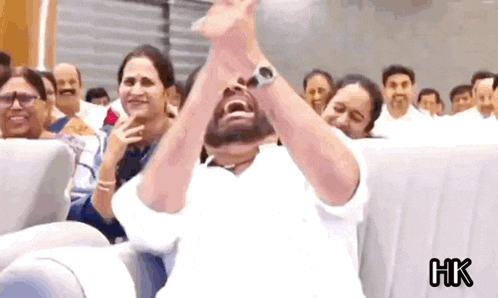 a man in a white shirt is sitting in front of a crowd with his hands in the air