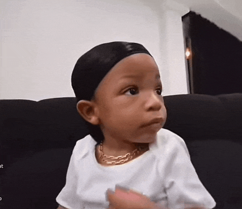 a little boy wearing a white shirt and a gold necklace is sitting on a couch