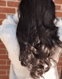 a woman with long dark hair is standing in front of a brick wall holding her hair .