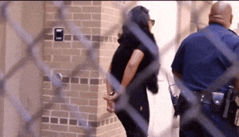 a woman in handcuffs is being escorted by two police officers through a chain link fence