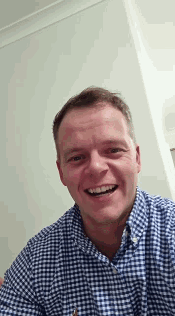 a man wearing a blue and white checkered shirt smiles for the camera