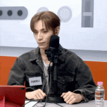 a man wearing a name tag that says haru sitting in front of a microphone