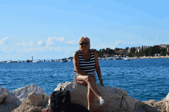 a woman sits on a rock near the water