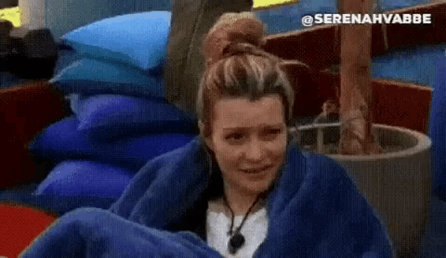 a woman wrapped in a blue blanket is sitting on a bed with pillows .