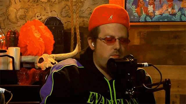 a man wearing a red hat and sunglasses is talking into a microphone .