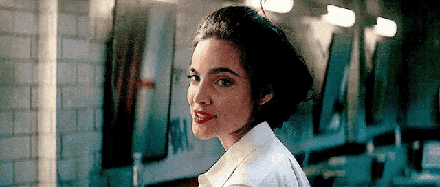 a woman wearing a white shirt and red lipstick is standing in a hallway .
