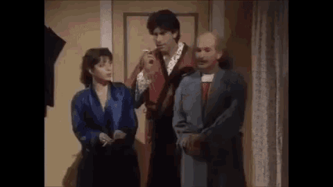 a man and a woman are standing next to each other in a room . the woman is smoking a cigarette .