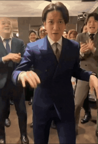 a man in a suit and tie is dancing in front of a group of men in suits and ties .