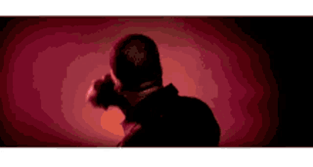 a man is standing in a dark room with a red background .