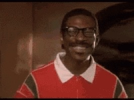 a man with glasses and a mustache is smiling in a red shirt .