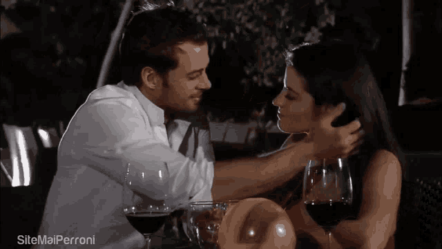 a man and a woman are kissing while sitting at a table with glasses of wine ..