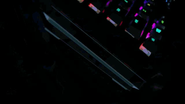 a black keyboard with rainbow colored keys is laying on a black surface