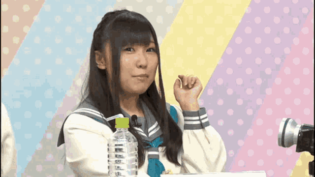 a girl in a school uniform is sitting in front of a microphone with a bottle of water next to her