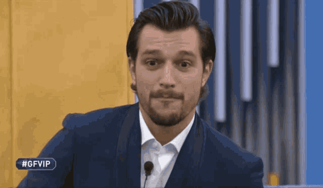 a man in a suit stands in front of a microphone with the hashtag #gfvip above him