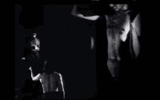 a black and white photo of a shirtless man sitting in a chair .
