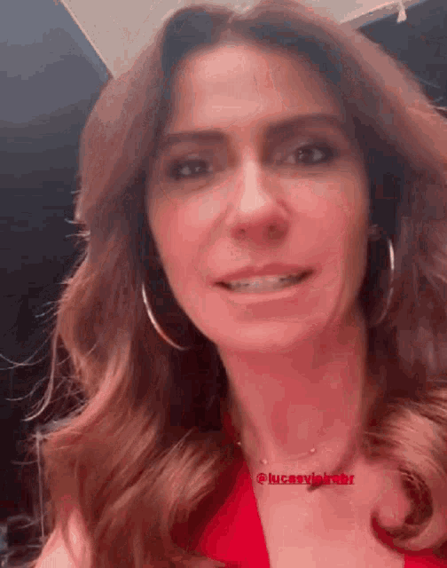 a woman wearing a red dress and hoop earrings is smiling and looking at the camera .