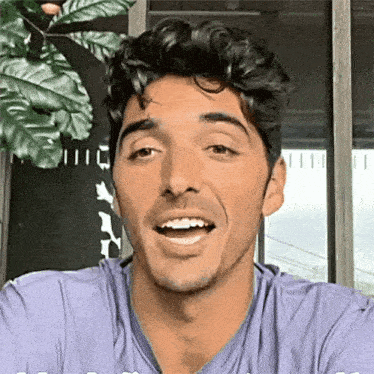 a man in a purple shirt is smiling while looking at the camera .