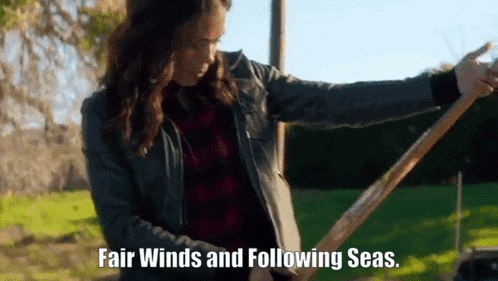 a woman in a leather jacket is holding a wooden stick with the words fair winds and following seas .