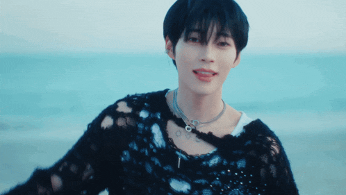 a young man wearing a black sweater and a necklace with the letter t on his neck