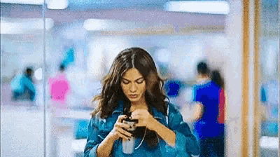 a woman is walking down a hallway while looking at her phone .