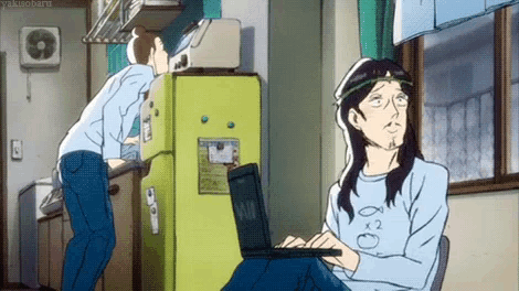 a man with long hair is using a laptop while another man looks on