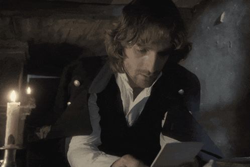a man in a dark room with a candle and a piece of paper in front of him