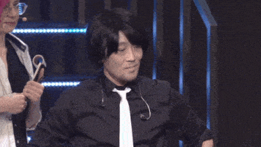 a man wearing a black shirt and tie gives a thumbs up