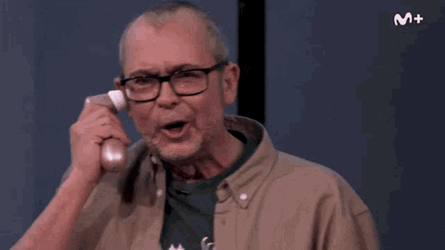 a man with glasses is talking on a phone with the letter m on the bottom right